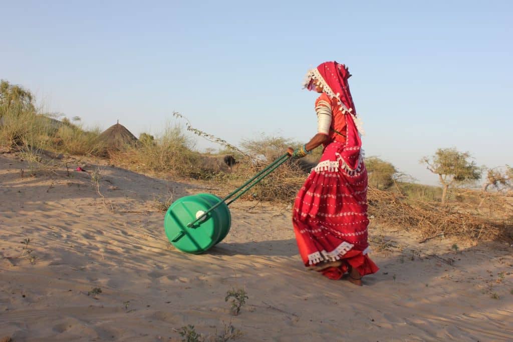 A woman carrying water by rolling the H2O (Help-2-Others) Wheel up the rough terrain to her home in Tharparkar. The ground bears the weight of the 40 litre Wheel, relieving her of the severe physical strain.