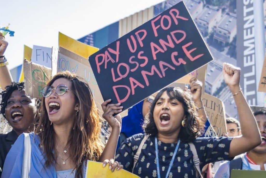 Girls advocating for loss and damage compensation at a protest, holding a sign saying "pay up for loss and damage"