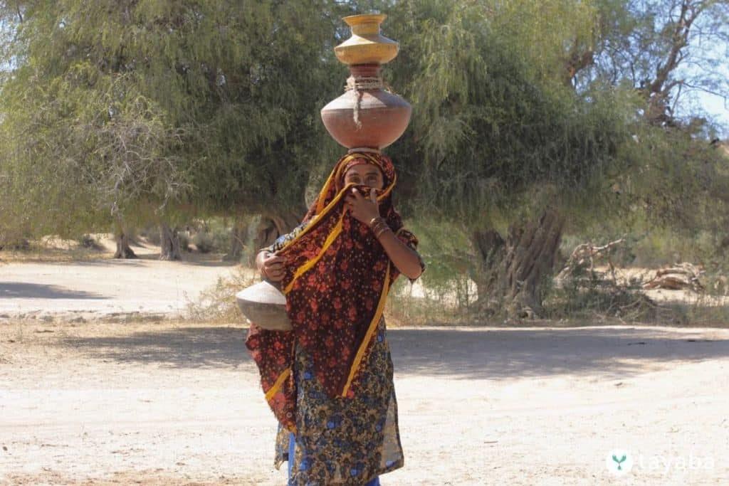 A woman headloads multiple containers. Head-loading has significant long-term physical ramifications on the women burdened with water collection, from spinal pain to health risks during pregnancy