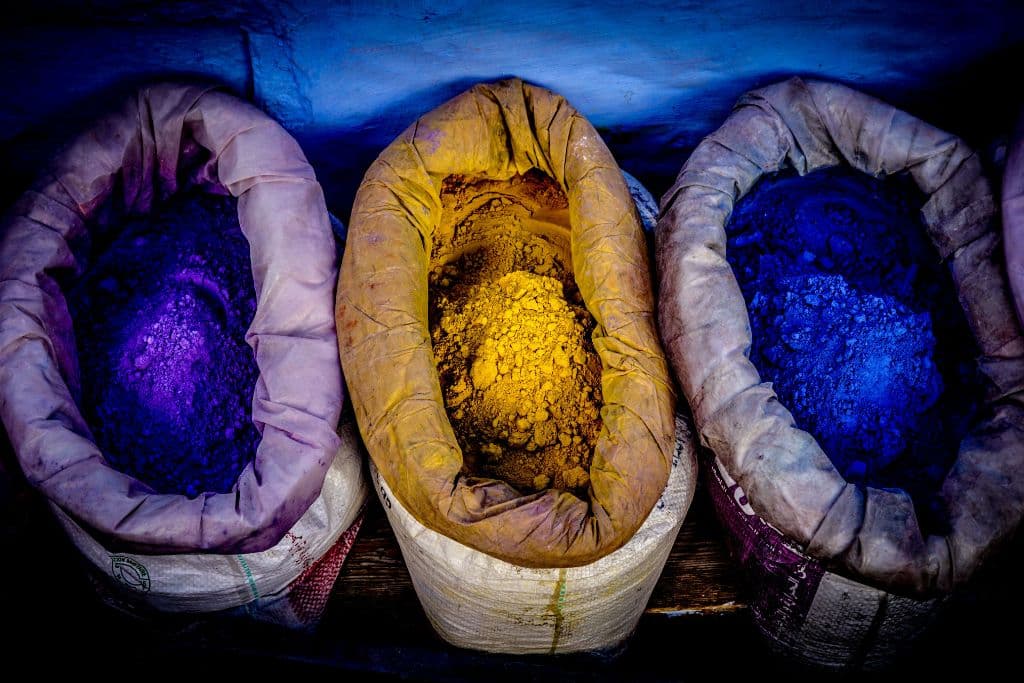 Three bags full of dye. One bag has purple dye, one bag has yellow dye and one bag has blue dye.