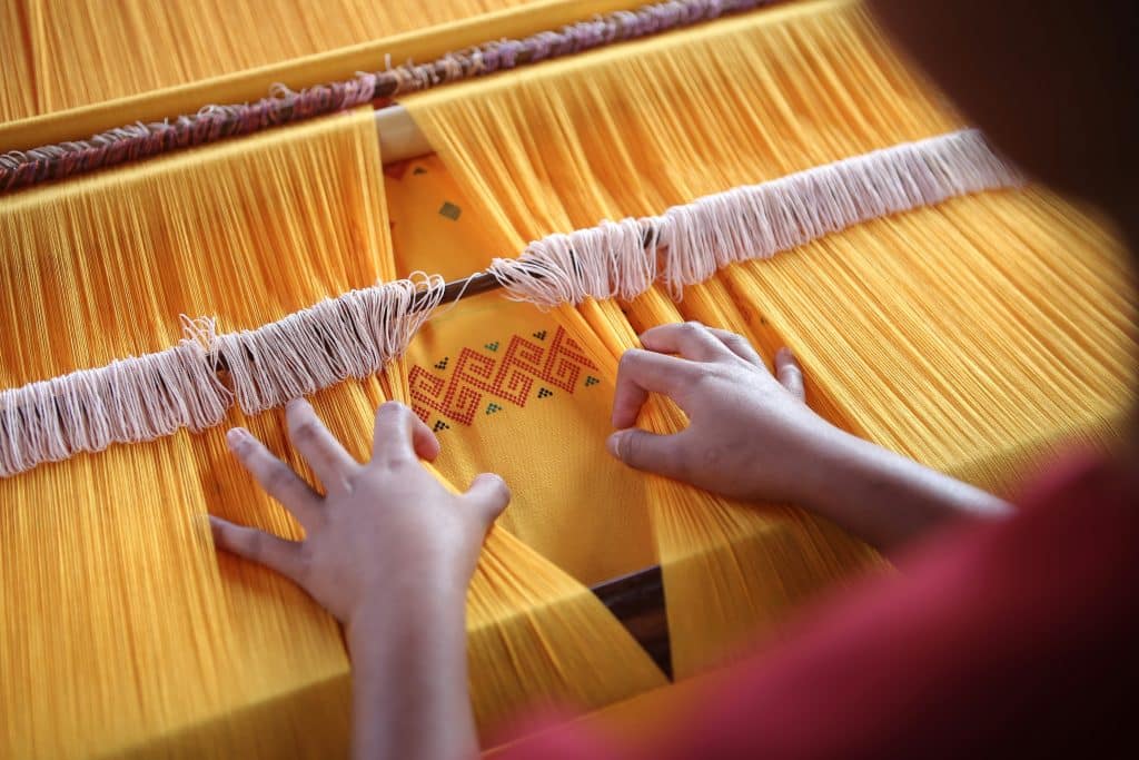 A person separates threads on a loom.